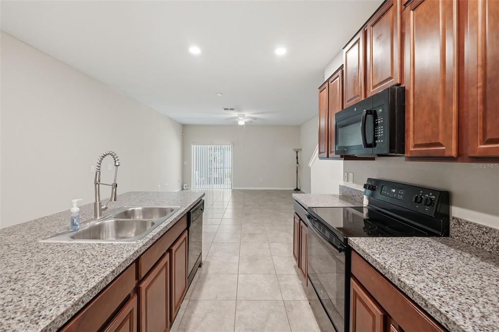 A kitchen with granite countertops, wooden cabinets, and stainless steel appliances overlooks an open living area — 10407 LAKE MONTAUK DRIVE, RIVERVIEW, FL