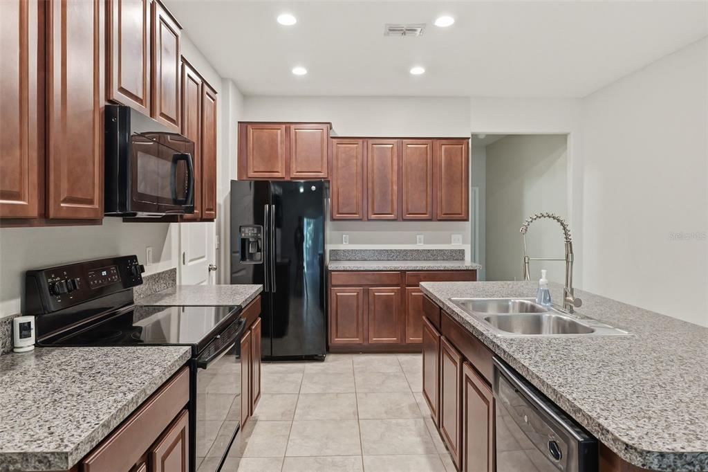 A kitchen features dark wood cabinets, granite countertops, black appliances, and a central island — 10407 LAKE MONTAUK DRIVE, RIVERVIEW, FL