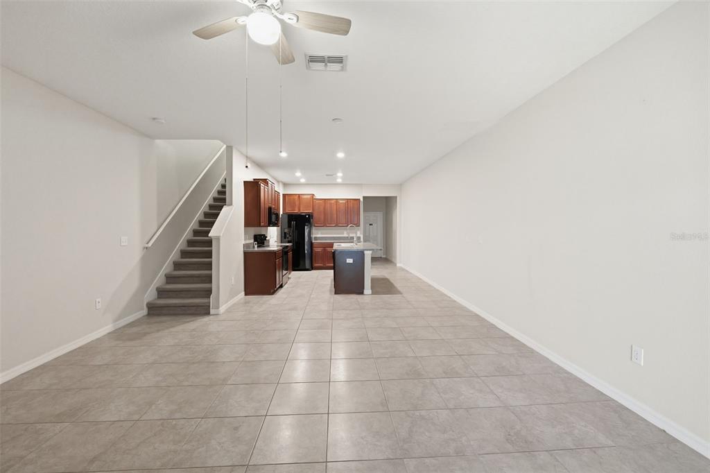 An open-concept living area features tile flooring, a staircase, and a kitchen with dark cabinetry — 10407 LAKE MONTAUK DRIVE, RIVERVIEW, FL