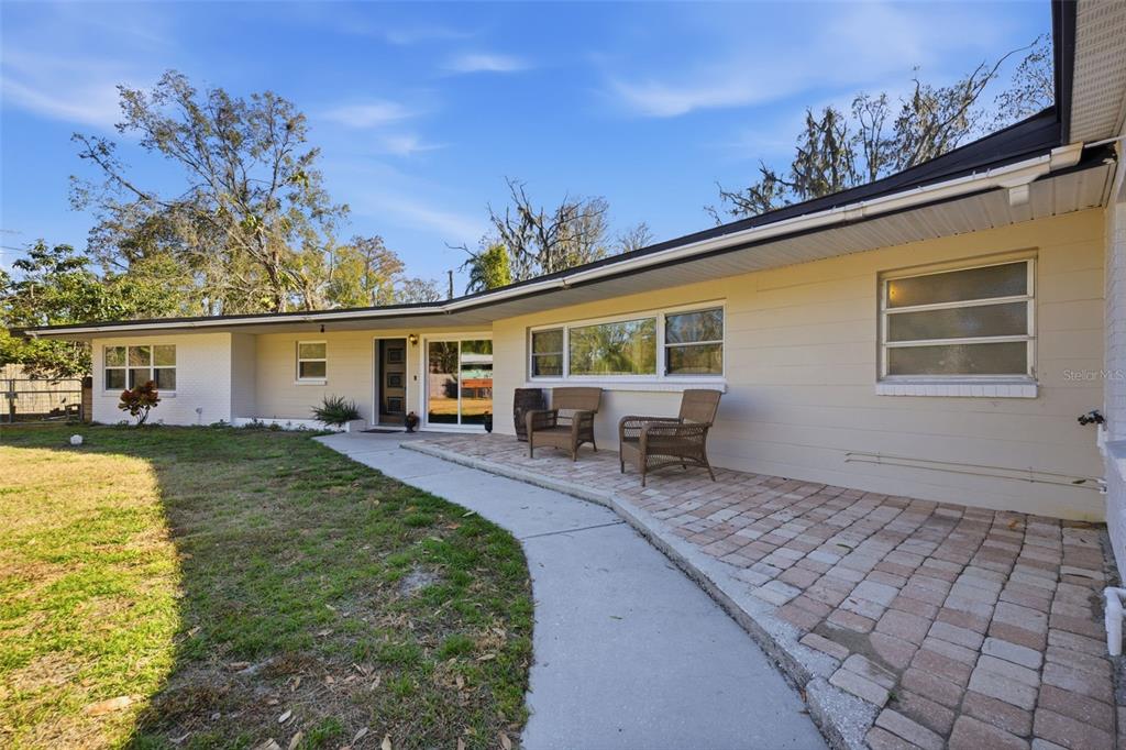 A single-story house exterior features a brick patio, a concrete walkway, and a lawn — 9214 RHEA DRIVE, ODESSA, FL