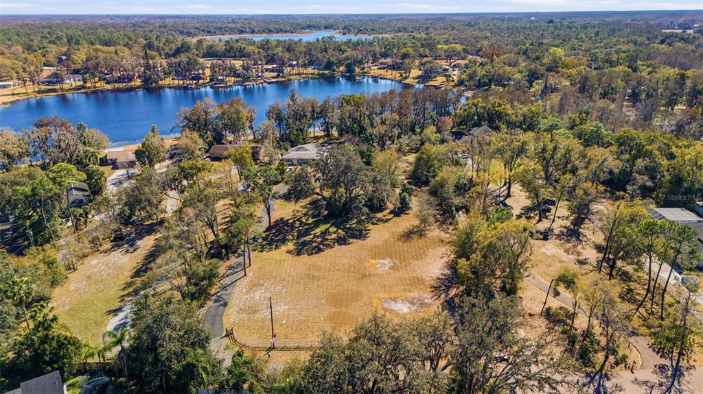 An aerial view shows a large, grassy lot surrounded by trees near a lake — 9214 RHEA DRIVE, ODESSA, FL