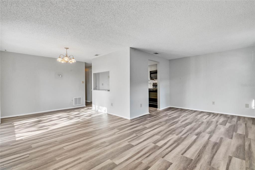 An open-concept living and dining area features light gray walls and wood-look vinyl flooring — 4907 LAKE RIDGE ROAD UNIT H, ORLANDO, FL