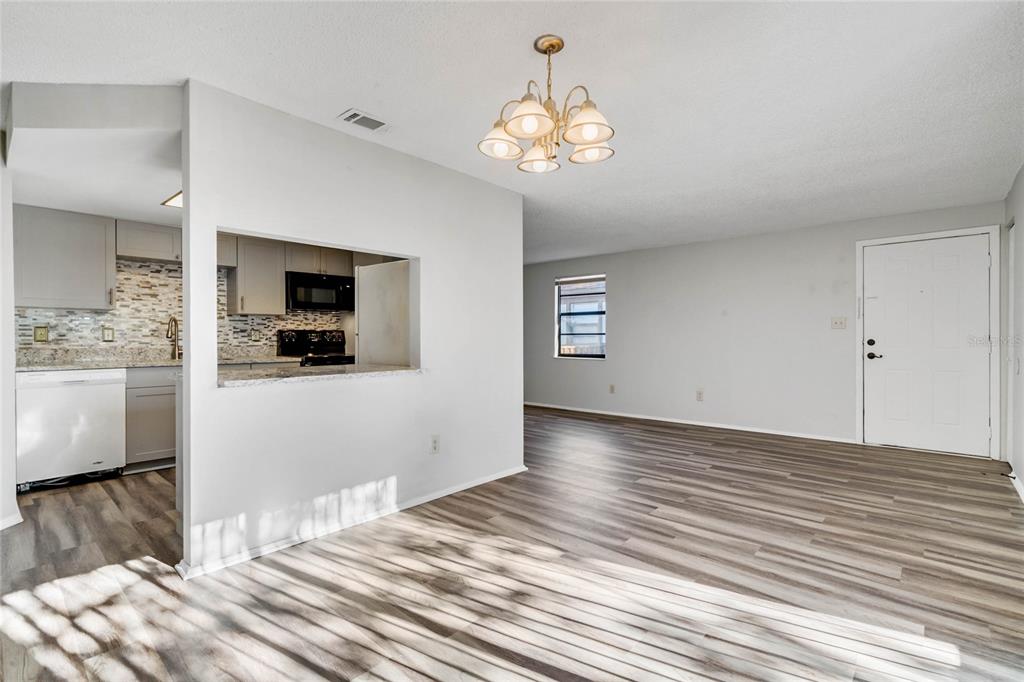 A living room with wood-look flooring, a chandelier, and a pass-through window to the kitchen — 4907 LAKE RIDGE ROAD UNIT H, ORLANDO, FL