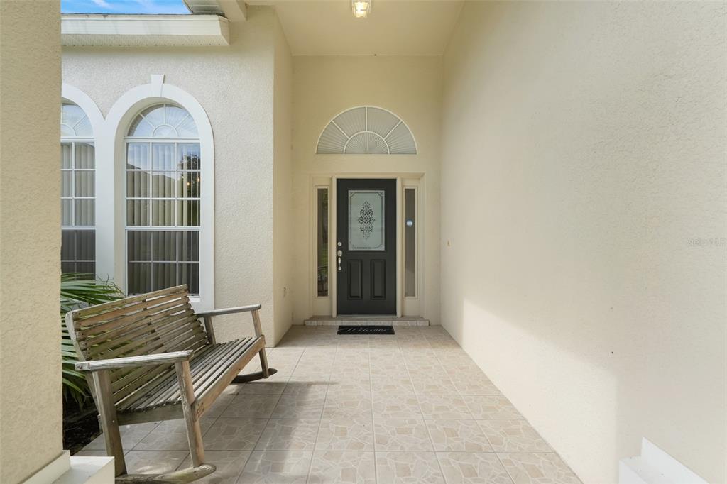 A covered entryway features a tiled floor, a wooden rocking bench, and a dark front door — 12900 CLOVERDALE LANE, CLERMONT, FL