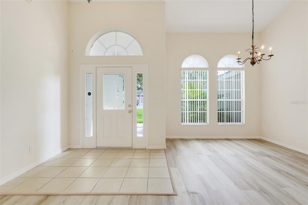 An entryway with tiled flooring transitions to light wood-look planks, featuring arched windows and doors — 12900 CLOVERDALE LANE, CLERMONT, FL