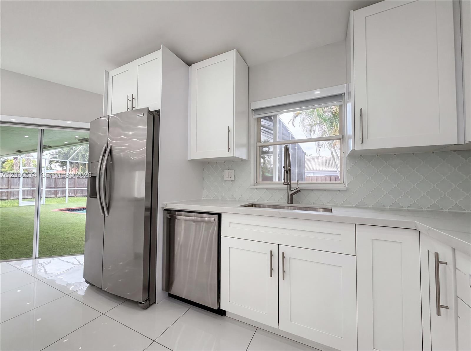 A modern kitchen features white cabinets, stainless steel appliances, and a view of a backyard — 16571 SW 145th Ave, Miami FL 33177, MIAMI, FL