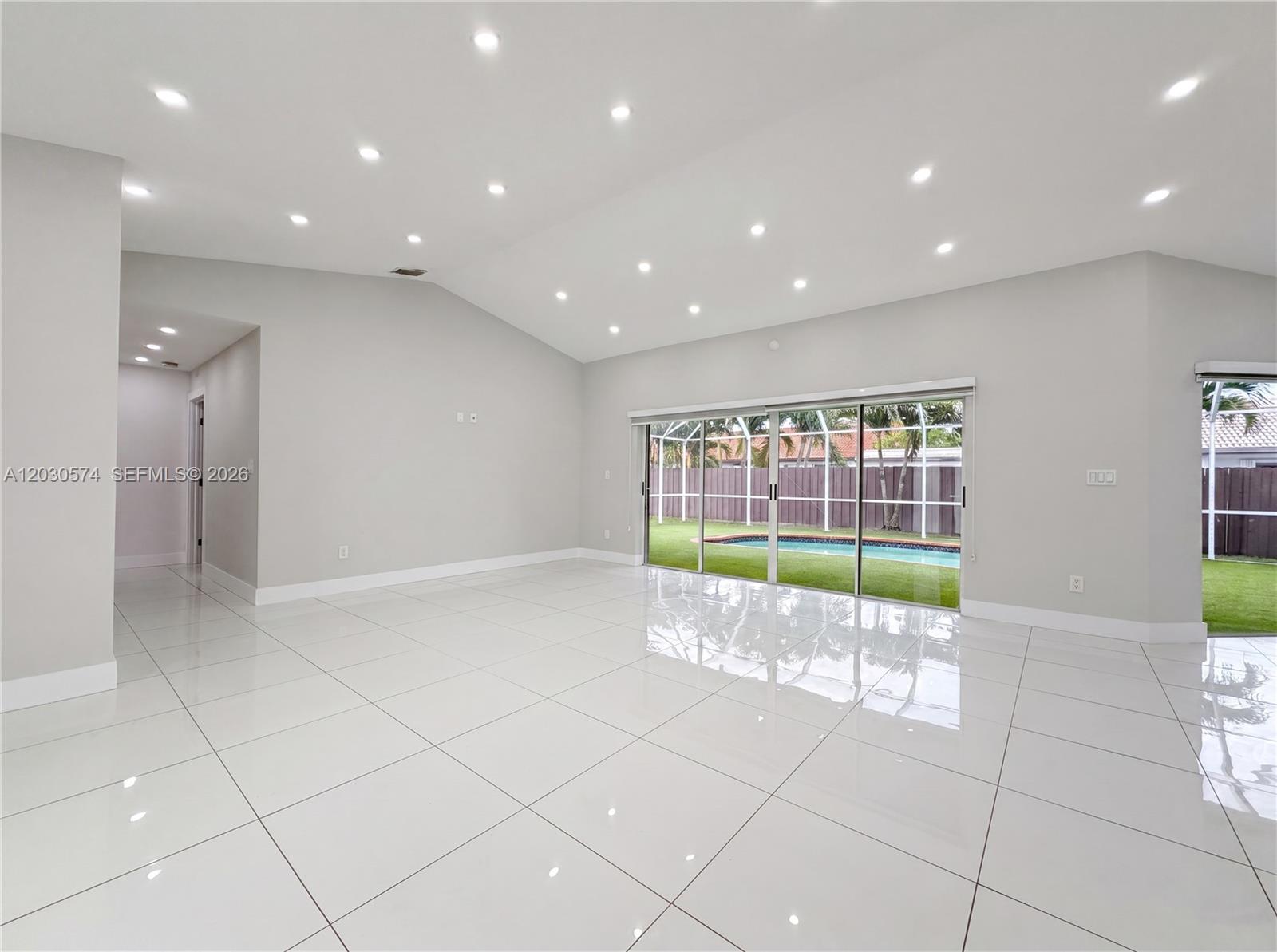 A bright, empty living room features white tile floors, recessed lighting, and sliding glass doors — 16571 SW 145th Ave, Miami FL 33177, MIAMI, FL
