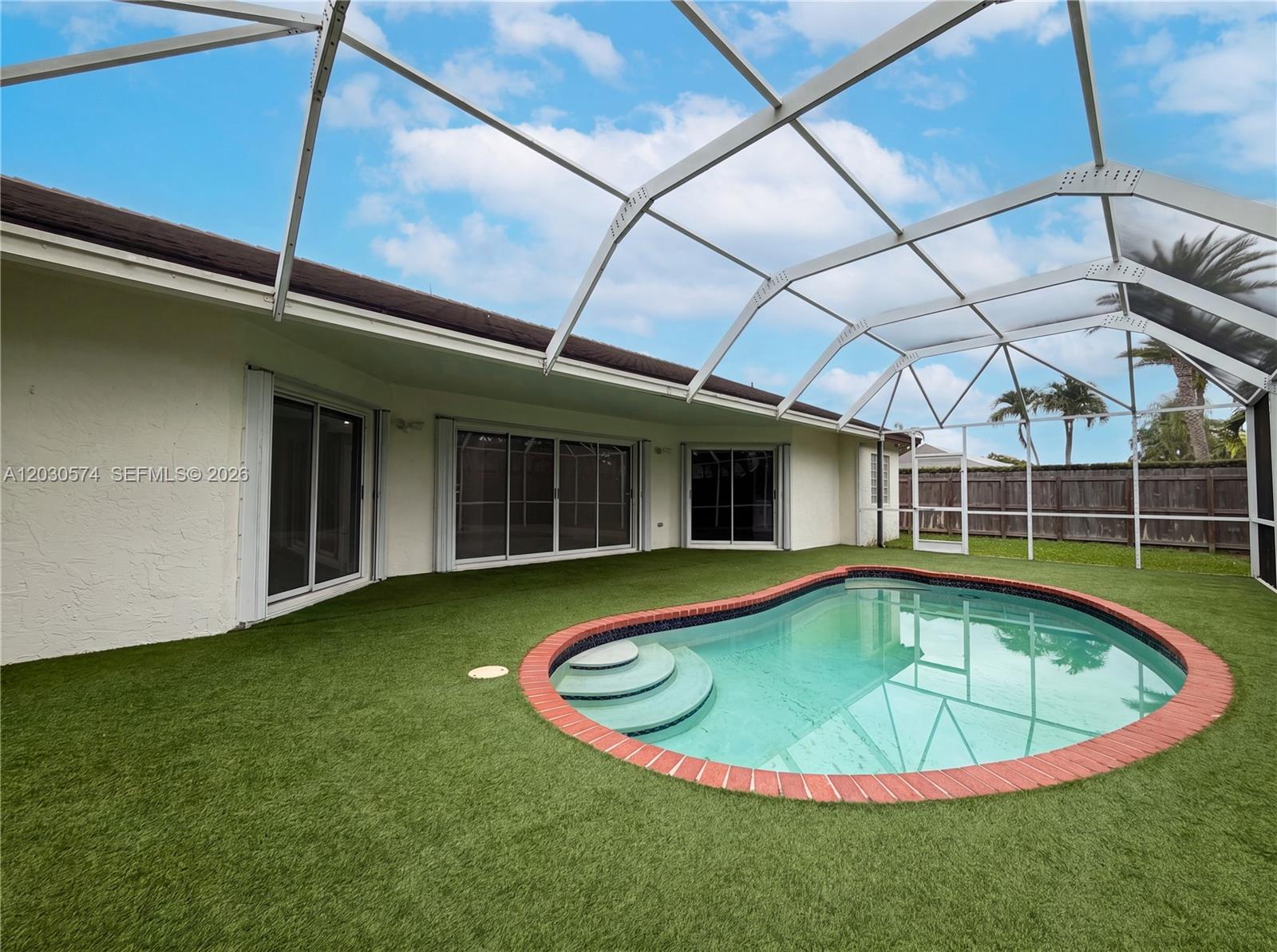 A screened-in patio features artificial turf surrounding a kidney-shaped pool with brick coping — 16571 SW 145th Ave, Miami FL 33177, MIAMI, FL