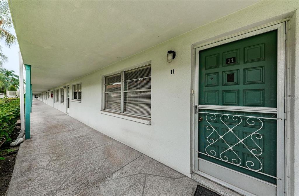 A covered exterior walkway leads to a green front door with a decorative metal screen — 5217 81ST STREET N UNIT 11, ST PETERSBURG, FL