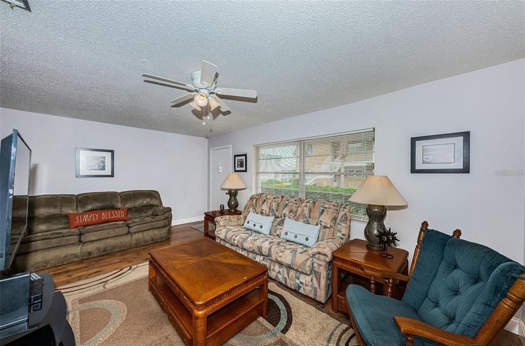 A living room features a patterned sofa, a brown couch, a teal armchair, and wood flooring — 5217 81ST STREET N UNIT 11, ST PETERSBURG, FL