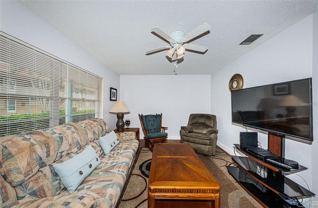 A living room features a patterned sofa, a wooden coffee table, and a wall-mounted television — 5217 81ST STREET N UNIT 11, ST PETERSBURG, FL