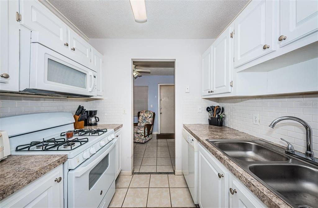 A galley kitchen features white cabinets, a gas stove, laminate countertops, and a double sink — 5217 81ST STREET N UNIT 11, ST PETERSBURG, FL