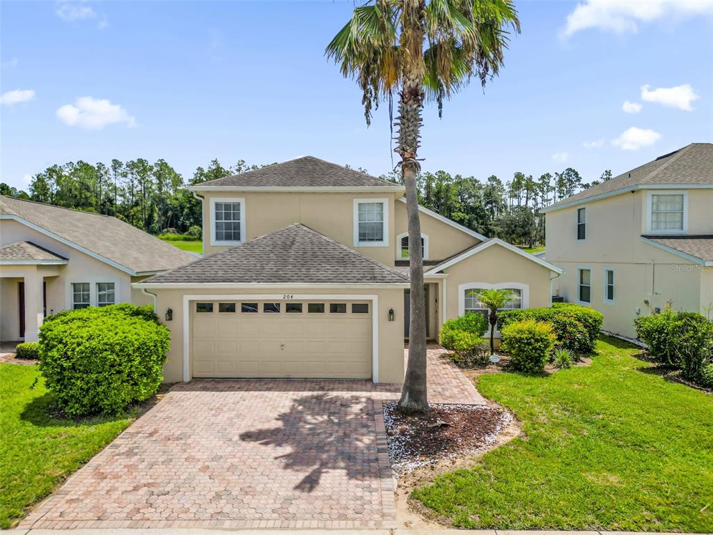 A two-story suburban house with a tan stucco exterior, a paved driveway, and a palm tree — 204 GLENEAGLES DRIVE, DAVENPORT, FL