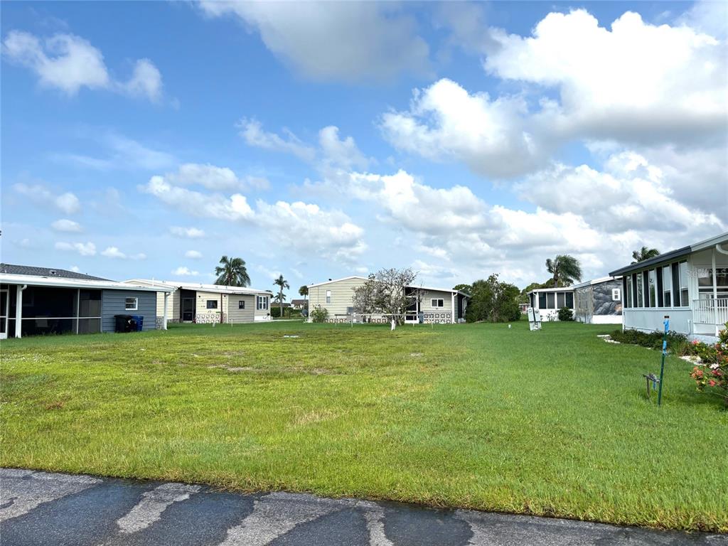A vacant grassy lot sits between two manufactured homes under a blue sky with clouds — 514 MADONNA, NORTH PORT, FL