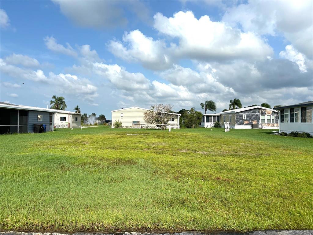 A vacant grassy lot sits between several manufactured homes under a cloudy blue sky — 514 MADONNA, NORTH PORT, FL