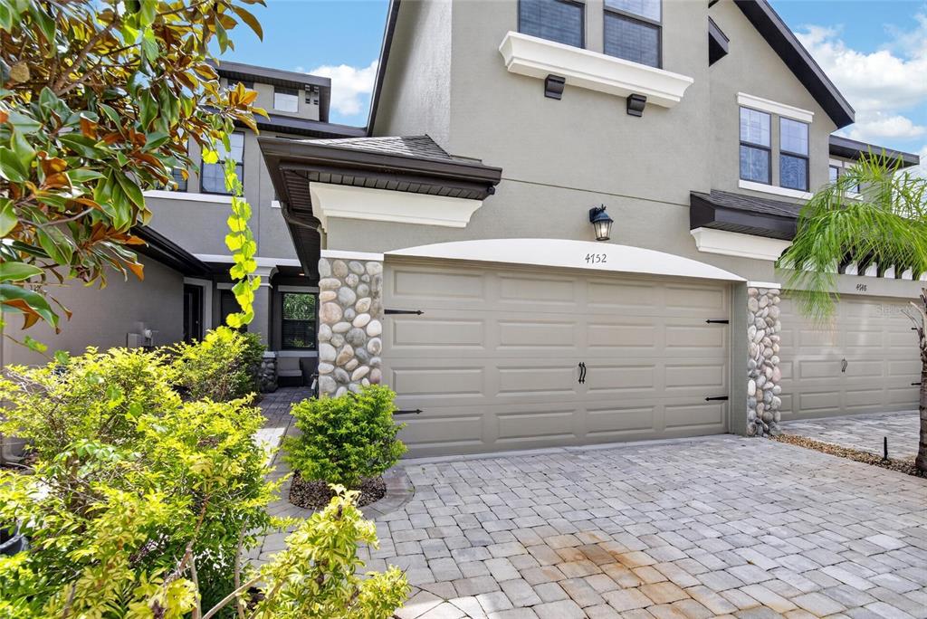 The exterior of a two-story townhouse features a stone-accented garage and a paved driveway — 4752 WANDERING WAY, WESLEY CHAPEL, FL