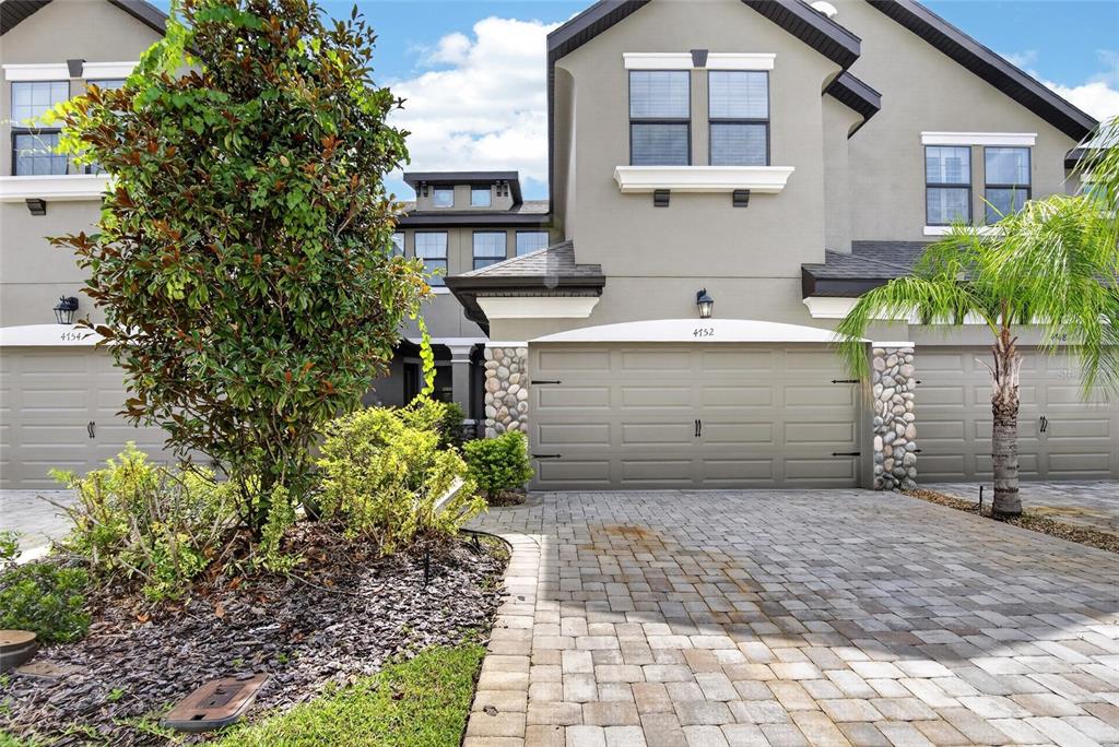 A covered front porch features a red door, a welcome mat, and a small chair — 4752 WANDERING WAY, WESLEY CHAPEL, FL