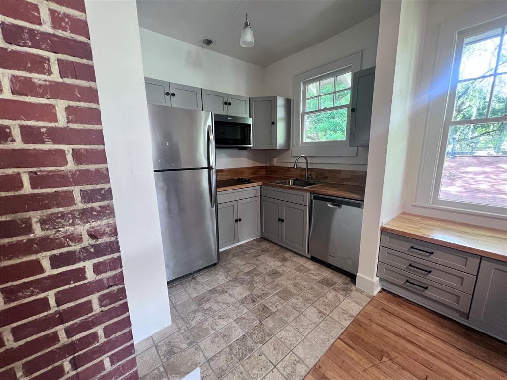A kitchen features gray cabinets, stainless steel appliances, wood countertops, and a brick accent wall — 204 NW 3RD STREET, GAINESVILLE, FL