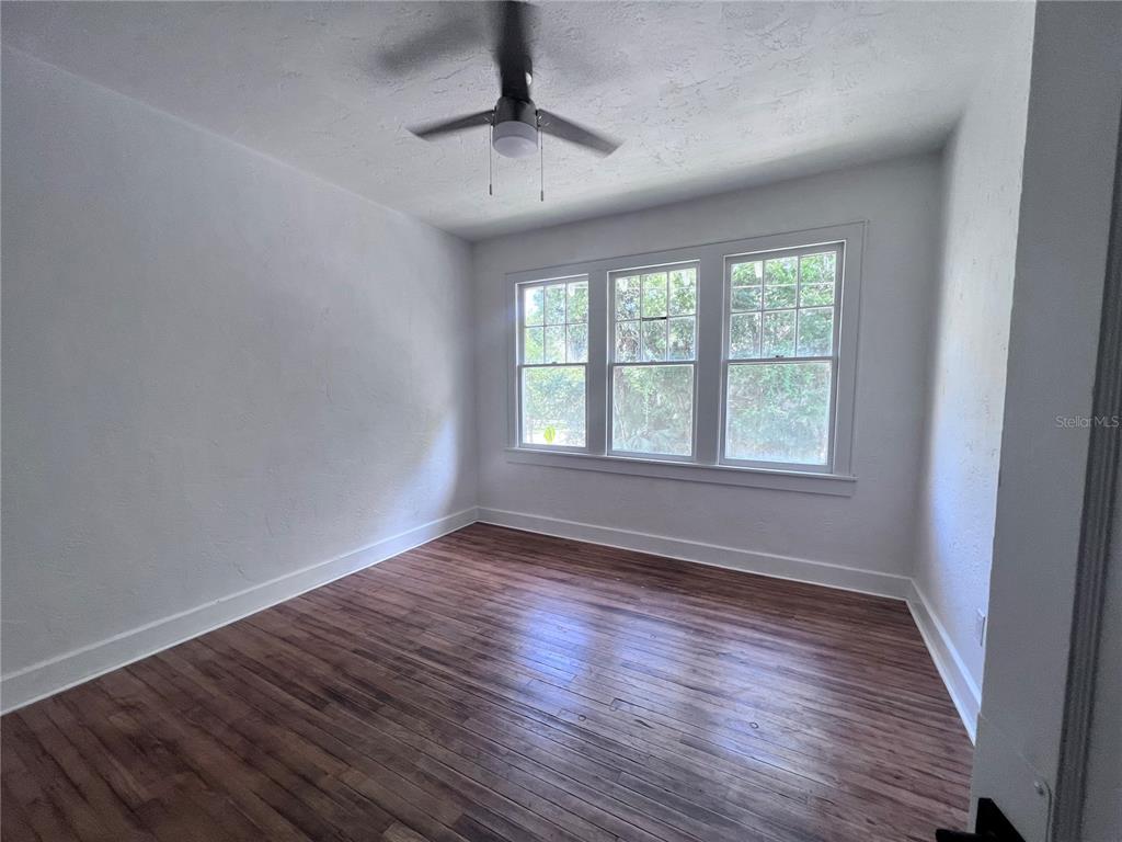 An empty bedroom features white walls, hardwood flooring, a ceiling fan, and three windows — 204 NW 3RD STREET, GAINESVILLE, FL