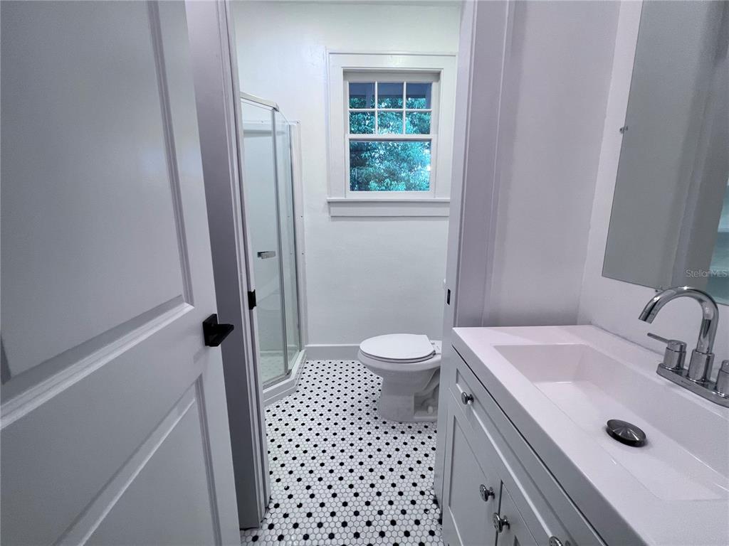 A bathroom features a white vanity, a corner glass shower, and black-and-white mosaic floor tiles — 204 NW 3RD STREET, GAINESVILLE, FL