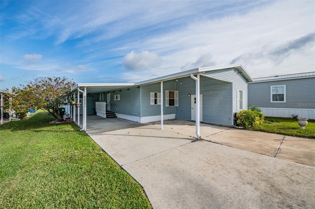 A light blue mobile home with a concrete driveway and a covered carport — 6827 S LAKE HENRY DRIVE NE, WINTER HAVEN, FL