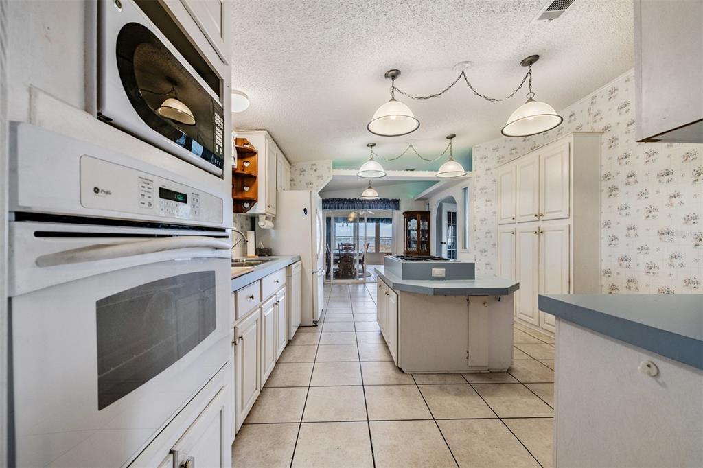 A kitchen features white cabinets, a central island, tile flooring, and pendant lighting — 6827 S LAKE HENRY DRIVE NE, WINTER HAVEN, FL