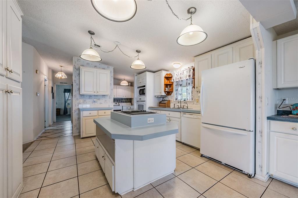 A kitchen features white cabinetry, a central island with a cooktop, and light-colored tile flooring — 6827 S LAKE HENRY DRIVE NE, WINTER HAVEN, FL