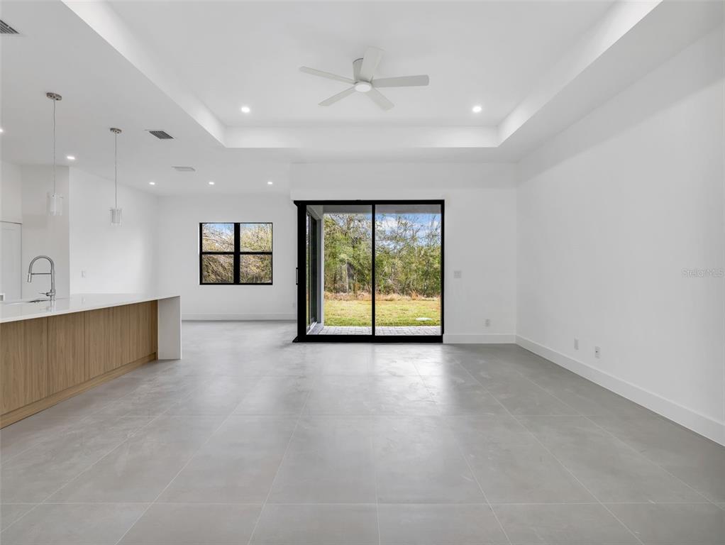 A modern open-concept living area features gray tile floors, a tray ceiling, and sliding glass doors — 6192 KAMBACH STREET, PORT CHARLOTTE, FL