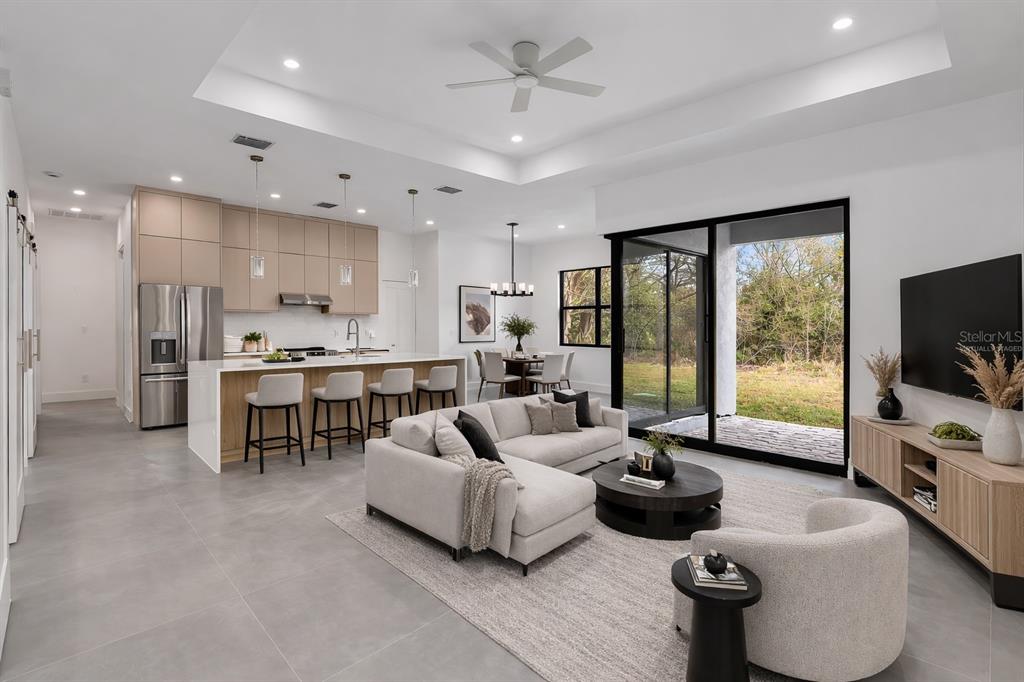An open-concept living room and kitchen with light wood cabinets, gray tile floors, and sliding doors — 6192 KAMBACH STREET, PORT CHARLOTTE, FL