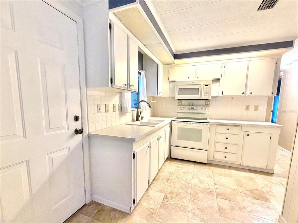 A kitchen with white cabinets, white appliances, a tiled backsplash, and light-colored tile flooring — 3335 S CITRUS CIRCLE UNIT GE, ZELLWOOD, FL