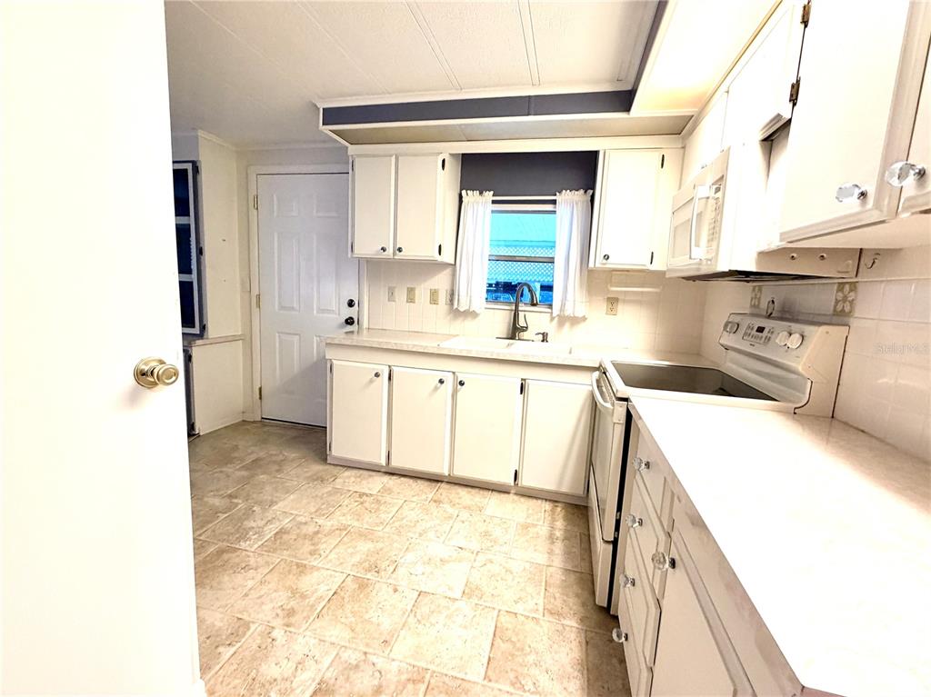 A kitchen features white cabinets, a white stove, a sink under a window, and tile flooring — 3335 S CITRUS CIRCLE UNIT GE, ZELLWOOD, FL