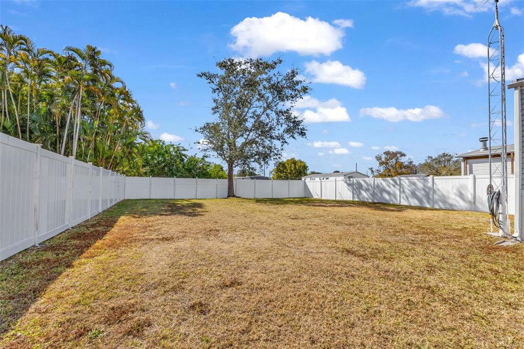 A fenced backyard features a large tree and dry grass under a blue sky — 1607 WOODLAWN AVENUE, PUNTA GORDA, FL