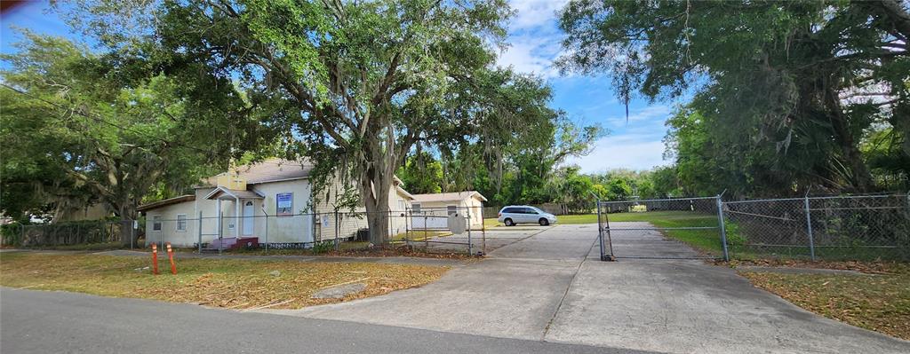 A light-colored building with a fenced parking lot sits under large trees — 1819 W 2ND STREET, SANFORD, FL
