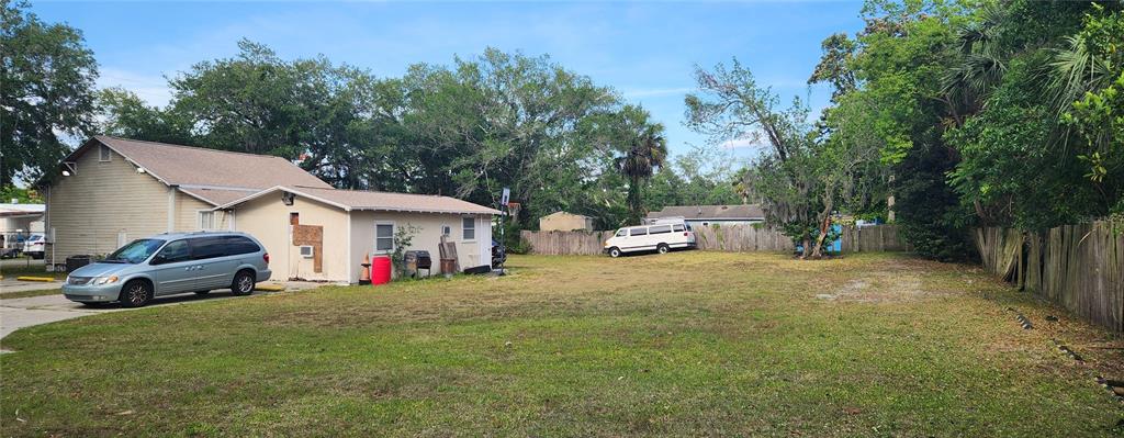 A large, grassy backyard features a light-colored house, a minivan, and a wooden fence — 1819 W 2ND STREET, SANFORD, FL