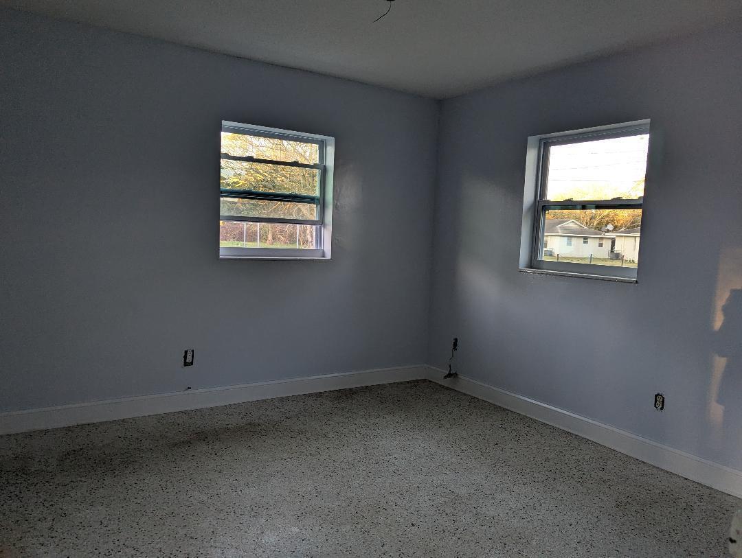 An empty bedroom features light blue walls, white trim, two windows, and speckled terrazzo flooring — 2736 Seneca Avenue, Fort Pierce FL 34945, FORT PIERCE, FL