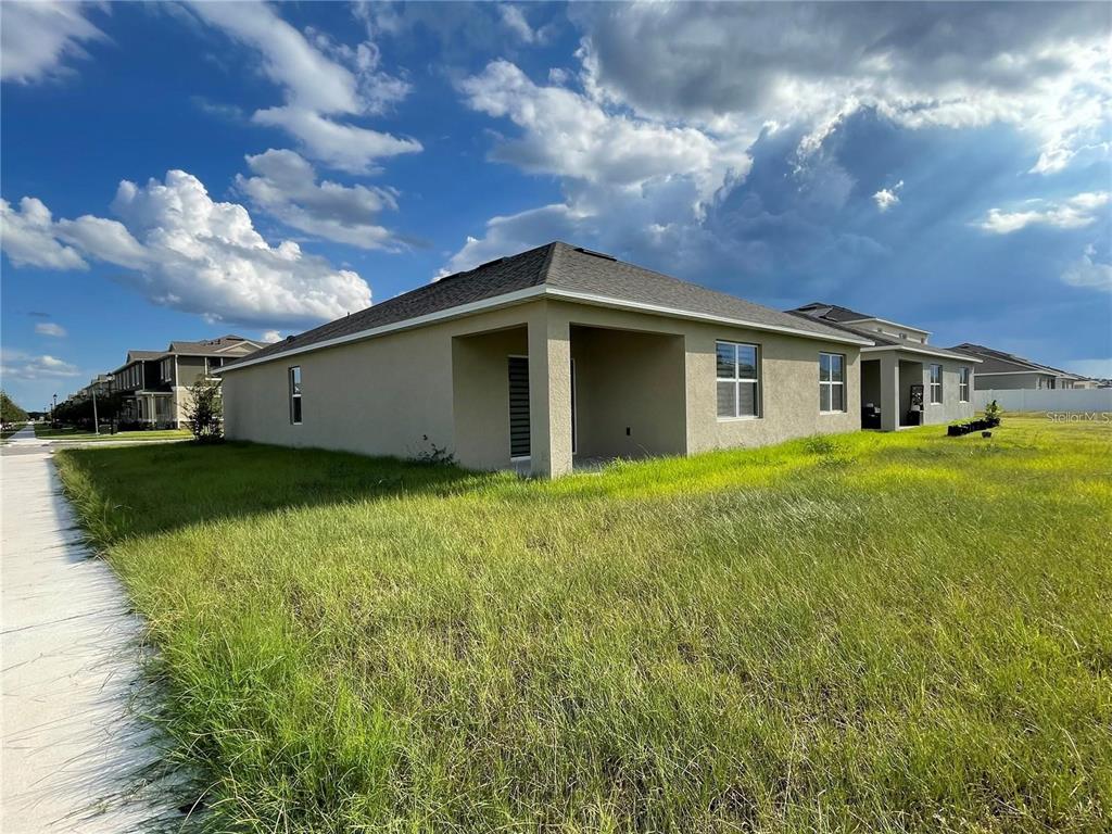 The exterior of a beige stucco house features a covered patio and a grassy yard — 1937 ARBOR MILL LANE, KISSIMMEE, FL