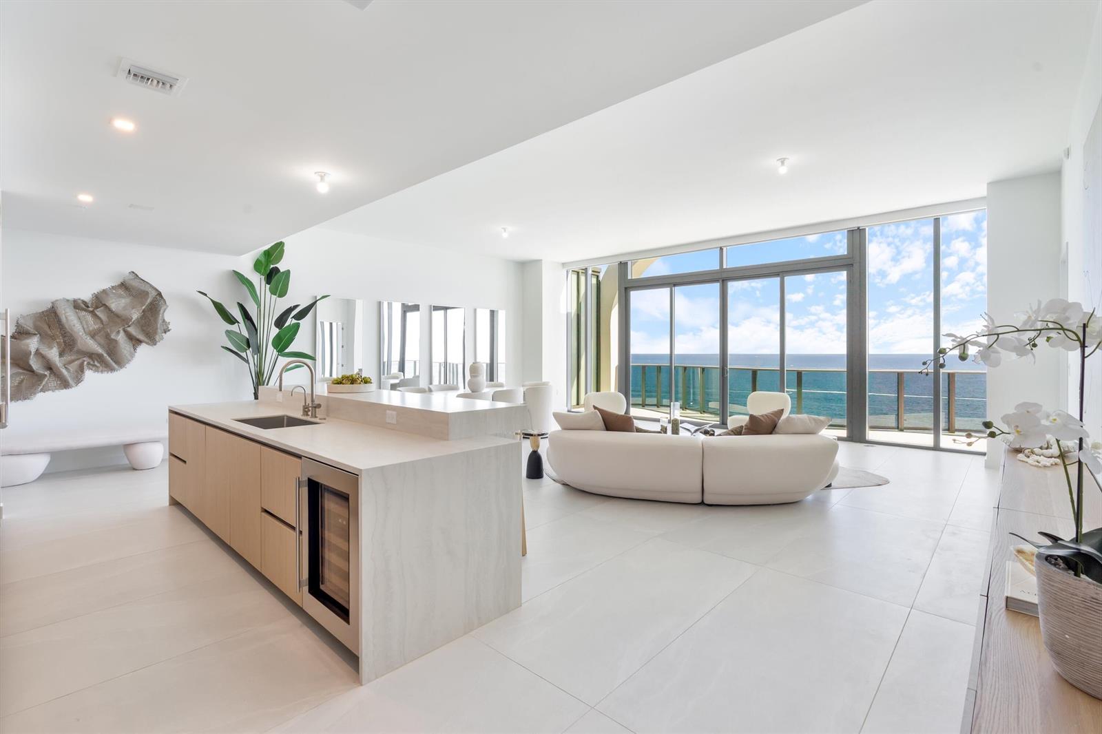 A modern open-concept kitchen and living area with ocean views through floor-to-ceiling glass doors — 900 N Ocean Boulevard, Pompano Beach FL 33062, POMPANO BEACH, FL