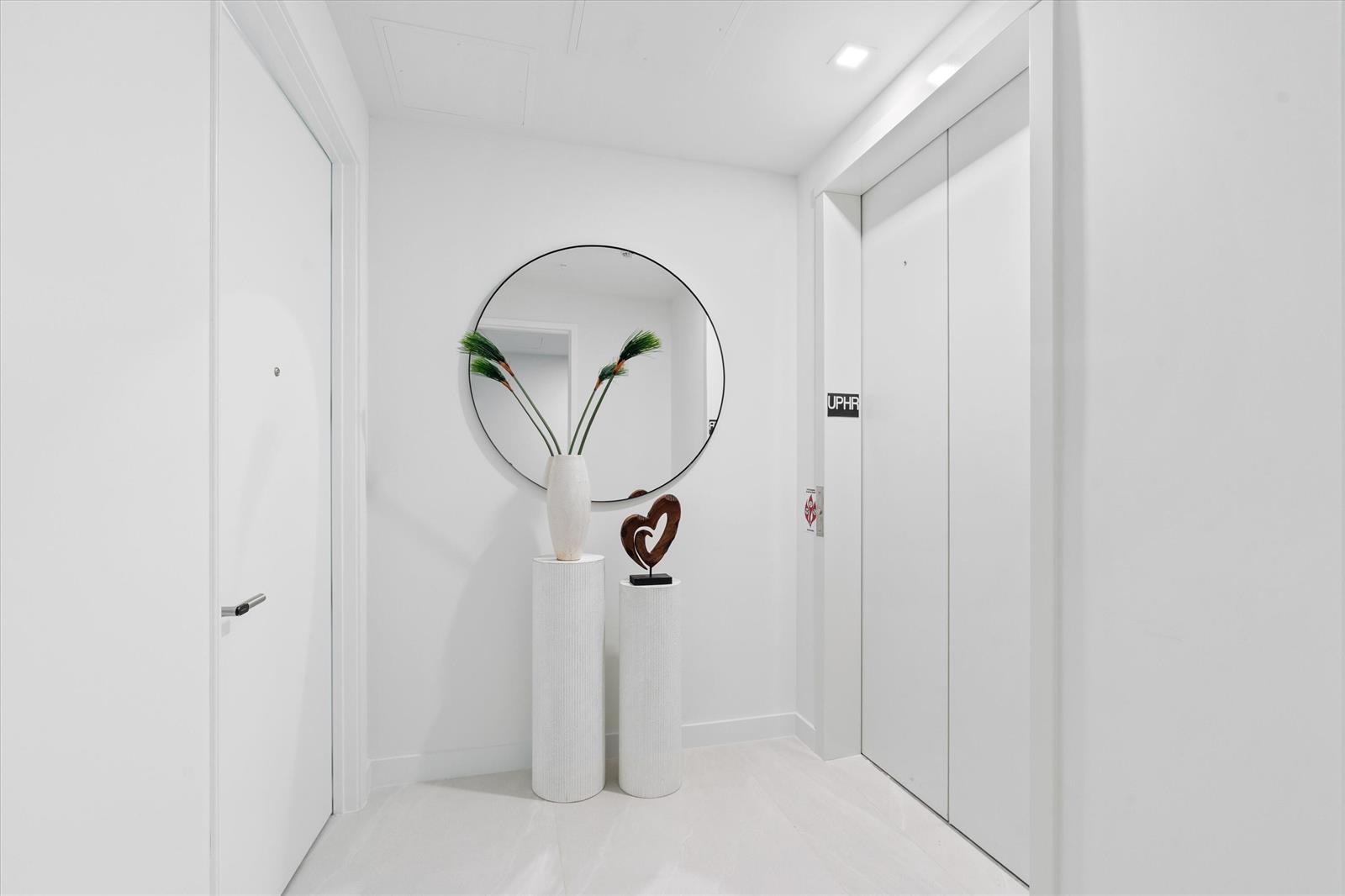 A minimalist white entryway features a round mirror, two pedestals with decor, and an elevator — 900 N Ocean Boulevard, Pompano Beach FL 33062, POMPANO BEACH, FL
