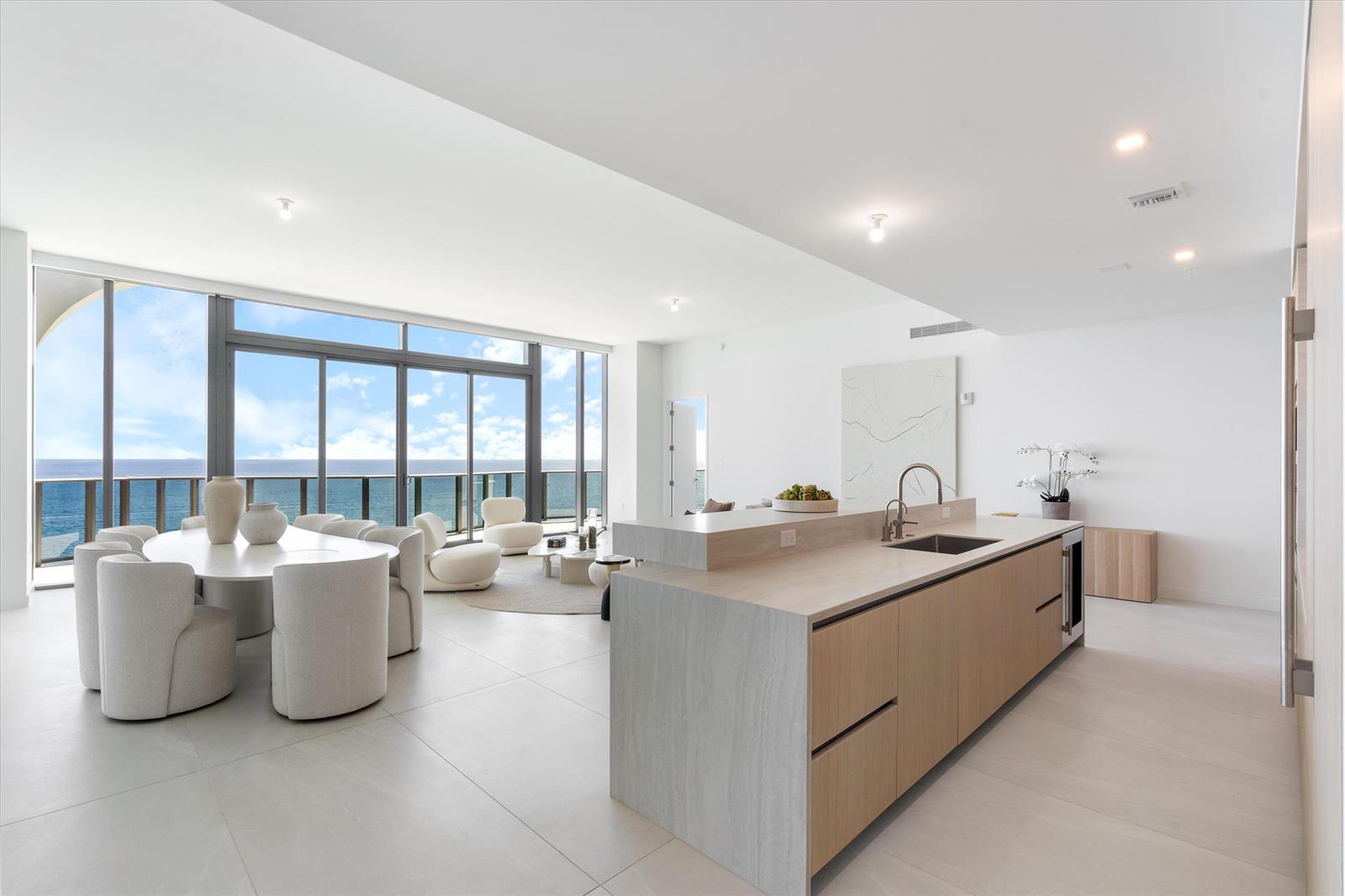 A modern open-plan kitchen and dining area features light wood cabinetry and floor-to-ceiling ocean views — 900 N Ocean Boulevard, Pompano Beach FL 33062, POMPANO BEACH, FL