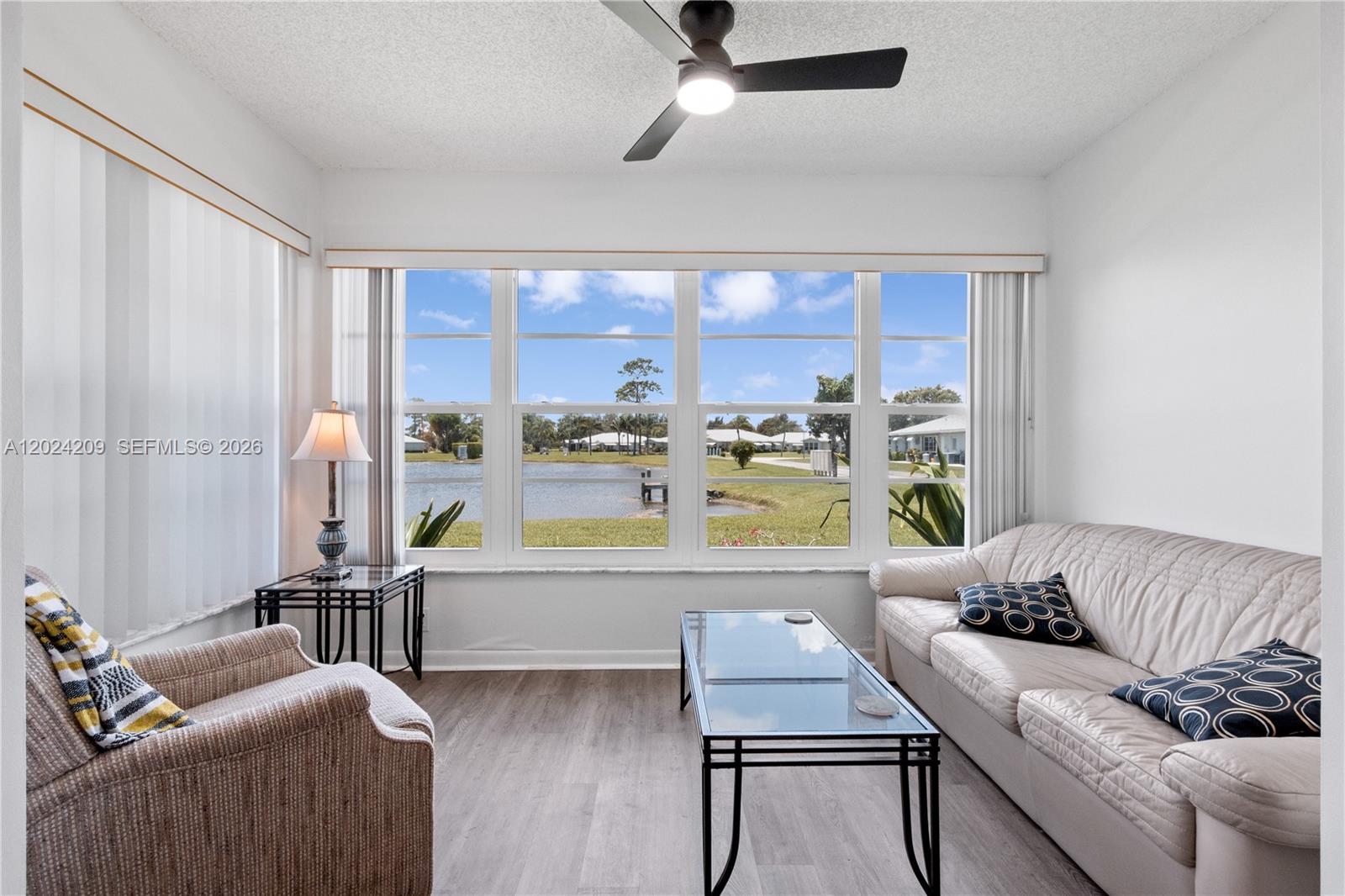A living room features a large window overlooking a lake, a sofa, and a chair — 14604 Canalview Dr # B, Delray Beach FL 33484, DELRAY BEACH, FL