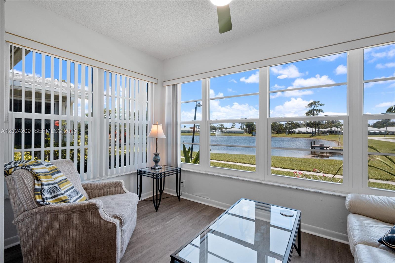 A sunroom features a glass coffee table, an armchair, and large windows overlooking a lake — 14604 Canalview Dr # B, Delray Beach FL 33484, DELRAY BEACH, FL
