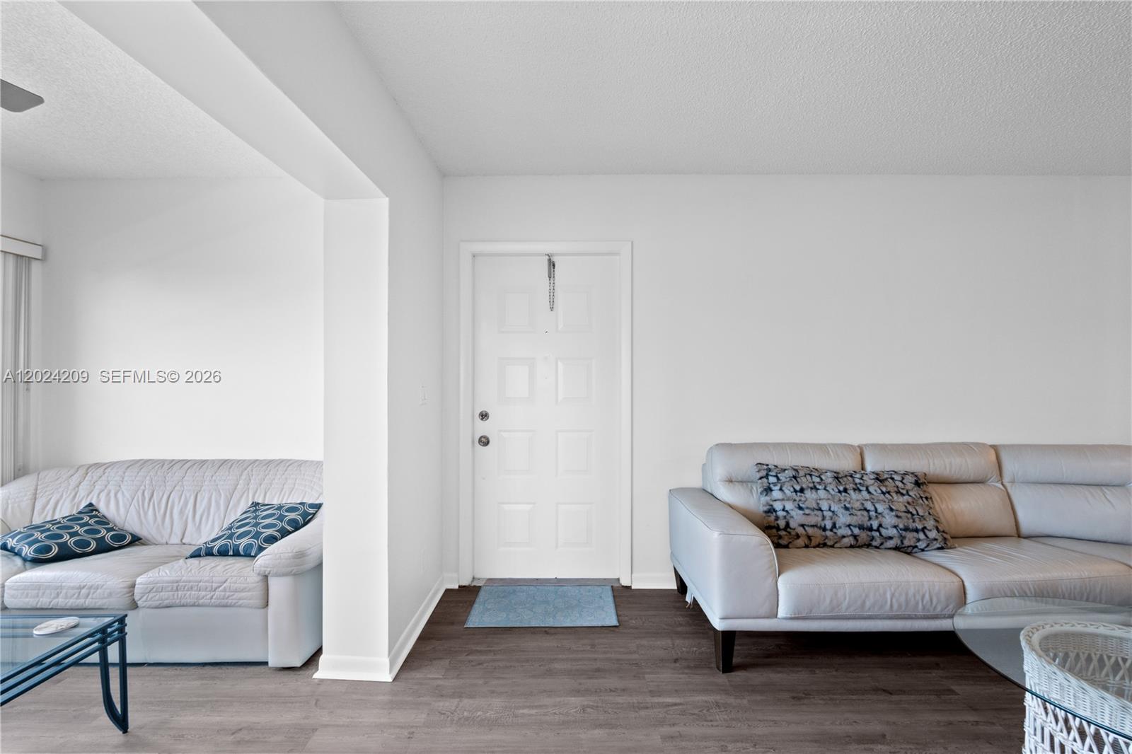 A living room features white walls, dark wood-look flooring, and two light-colored leather sofas — 14604 Canalview Dr # B, Delray Beach FL 33484, DELRAY BEACH, FL