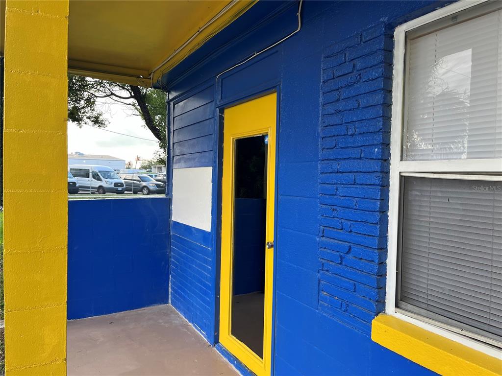 The exterior of a building features a blue brick wall, a yellow door, and a porch — 805 FERGUSON DRIVE, ORLANDO, FL