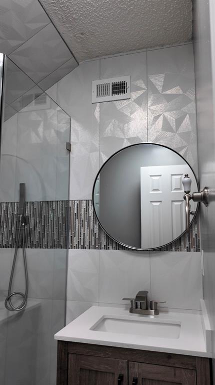 A bathroom vanity with a white countertop, round mirror, and tiled wall with glass shower — 3276 WOODGLEN DRIVE, ORANGE PARK, FL