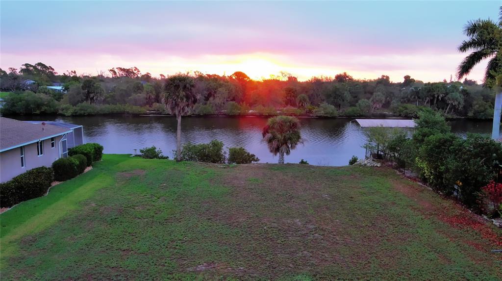 An elevated view of a grassy backyard overlooking a canal at sunset — 3190 LAKE VIEW BOULEVARD, PORT CHARLOTTE, FL