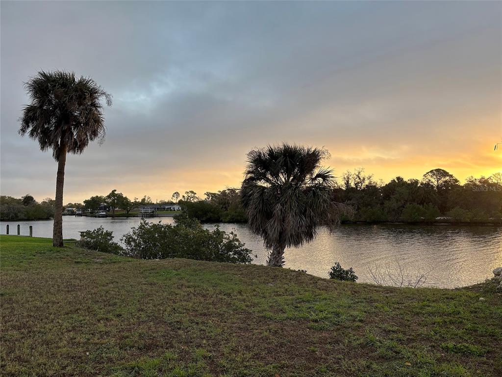 A grassy lawn overlooks a calm body of water with two palm trees at sunset — 3190 LAKE VIEW BOULEVARD, PORT CHARLOTTE, FL