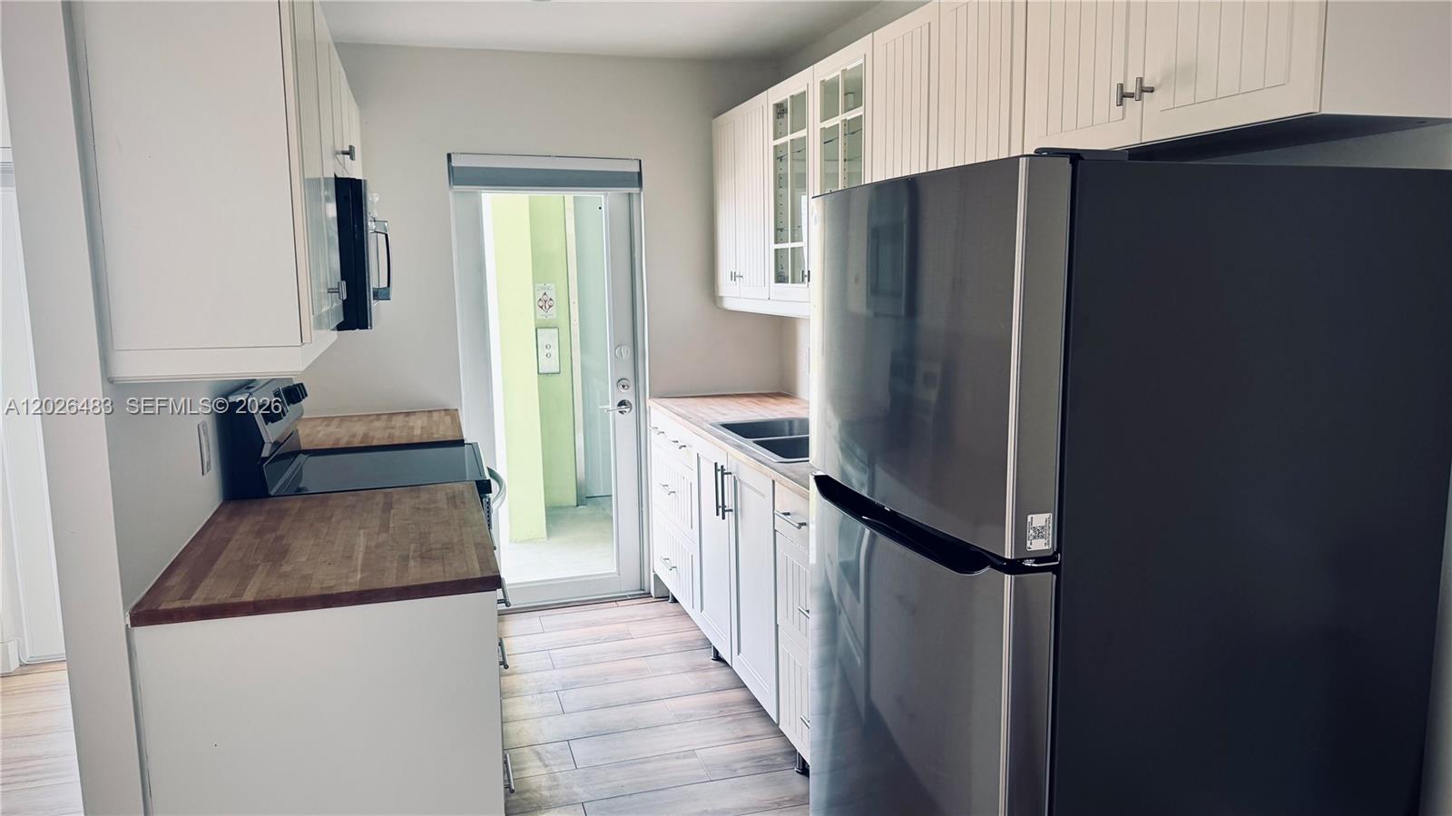A kitchen features white cabinetry, wood countertops, stainless steel appliances, and a glass exterior door — 363 Washington Ave # 52, Miami Beach FL 33139, MIAMI BEACH, FL