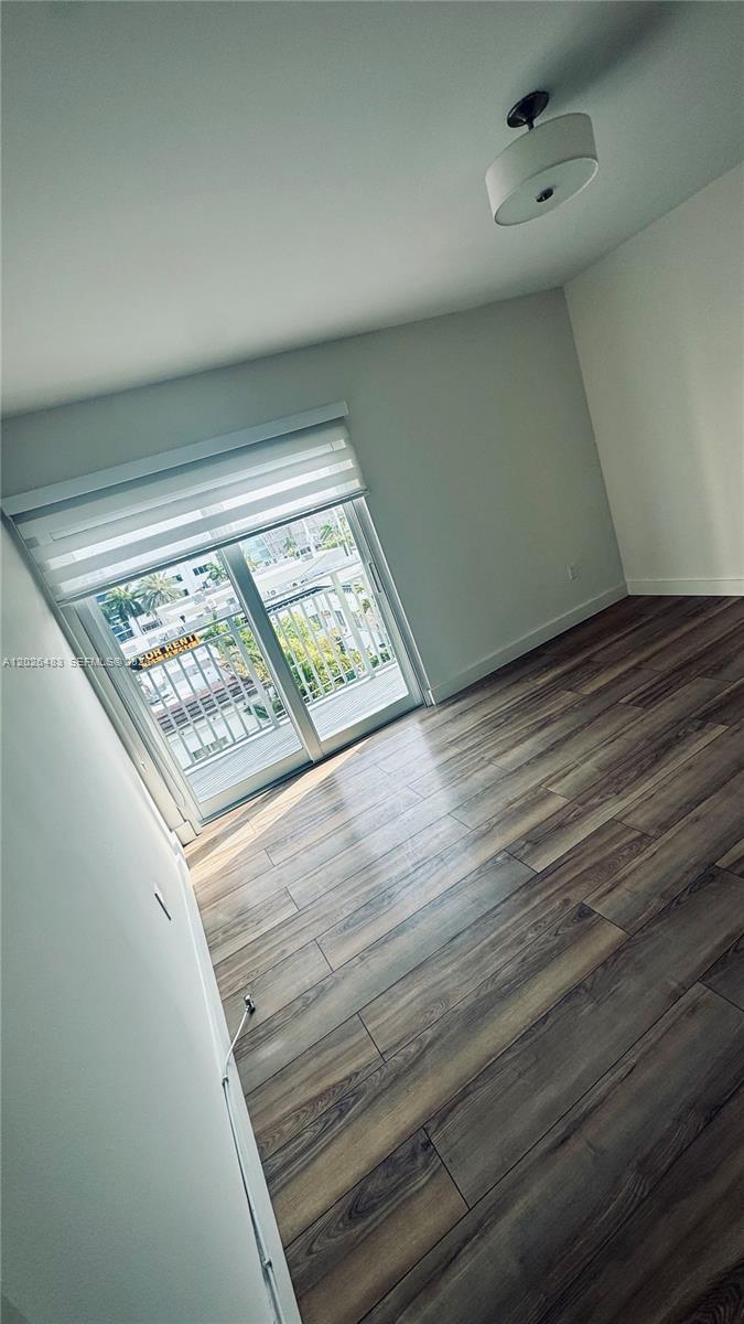 An empty room features wood-look flooring, a ceiling light fixture, and a sliding glass door — 363 Washington Ave # 52, Miami Beach FL 33139, MIAMI BEACH, FL