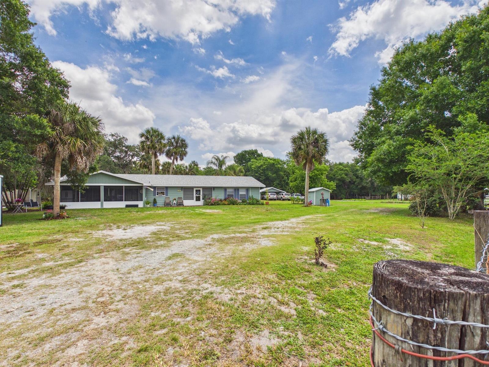 A light green single-story house sits on a grassy lot with palm trees and outbuildings — 220 SW 67th Drive, Okeechobee FL 34974, OKEECHOBEE, FL
