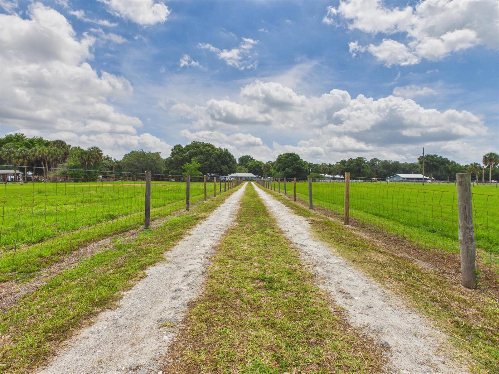 A gravel driveway leads through a fenced green pasture toward a house under a cloudy sky — 220 SW 67th Drive, Okeechobee FL 34974, OKEECHOBEE, FL